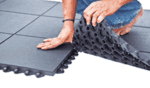 Extra large image showing a person installing rubber floor tiles on a grey tiled surface.