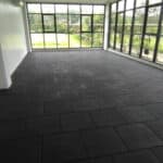 Dark grey tile flooring in a bright, sunlit room with large windows and lush greenery outside.