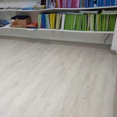 Light wood flooring installed in an office with colorful files on shelves behind.