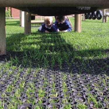 Paving grass growing through ground grid underneath outdoor play area with children.